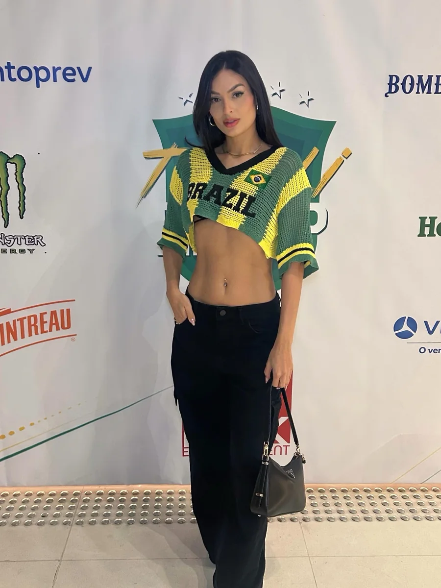 Débora Xavier com camisa do Brasil e calça preta diante do painel do evento Tivoli Fire Up
