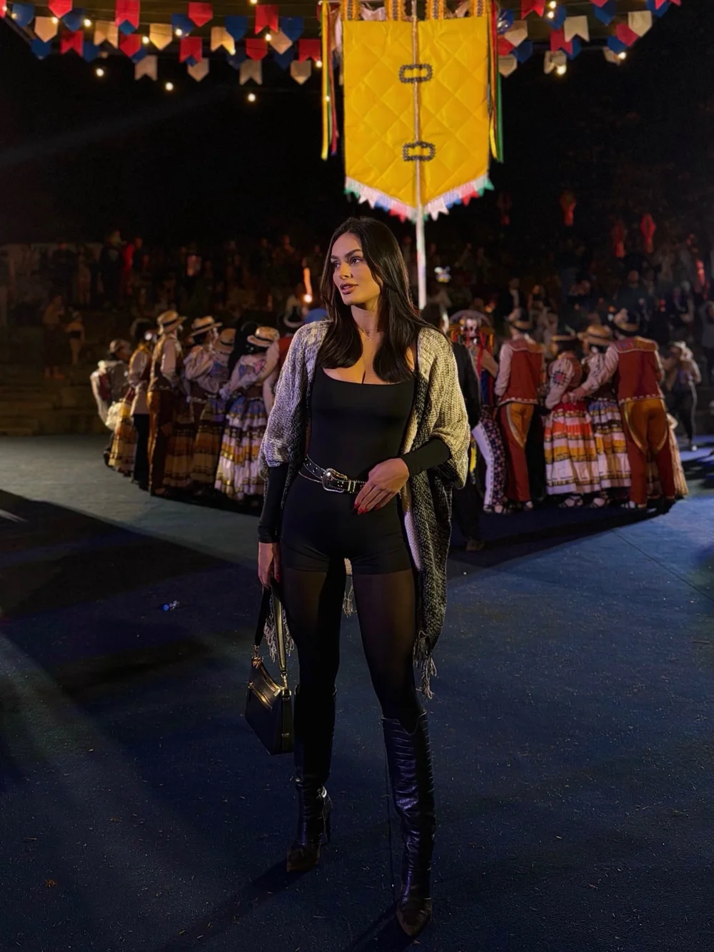 Débora Xavier de roupa preta e colete em pé em uma arena de rodeio à noite